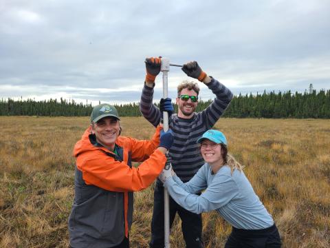 Cameron Kuhle (center), with advisor Dr. Eric Klein (left) and fellow graduate student Leah Boccignone (right), extracting a peat sediment core from a Kenai Peninsula peatland for analyses of carbon content and its loss during fire.  Courtesy of Cameron Kuhle.